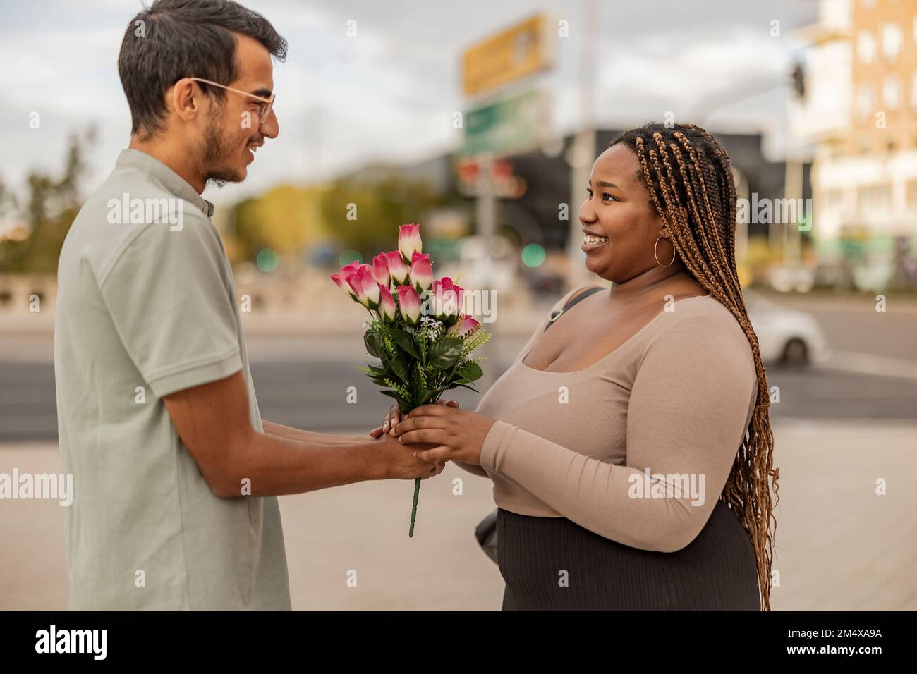 Young man giving bouquet of flowers to girlfriend at footpath Stock