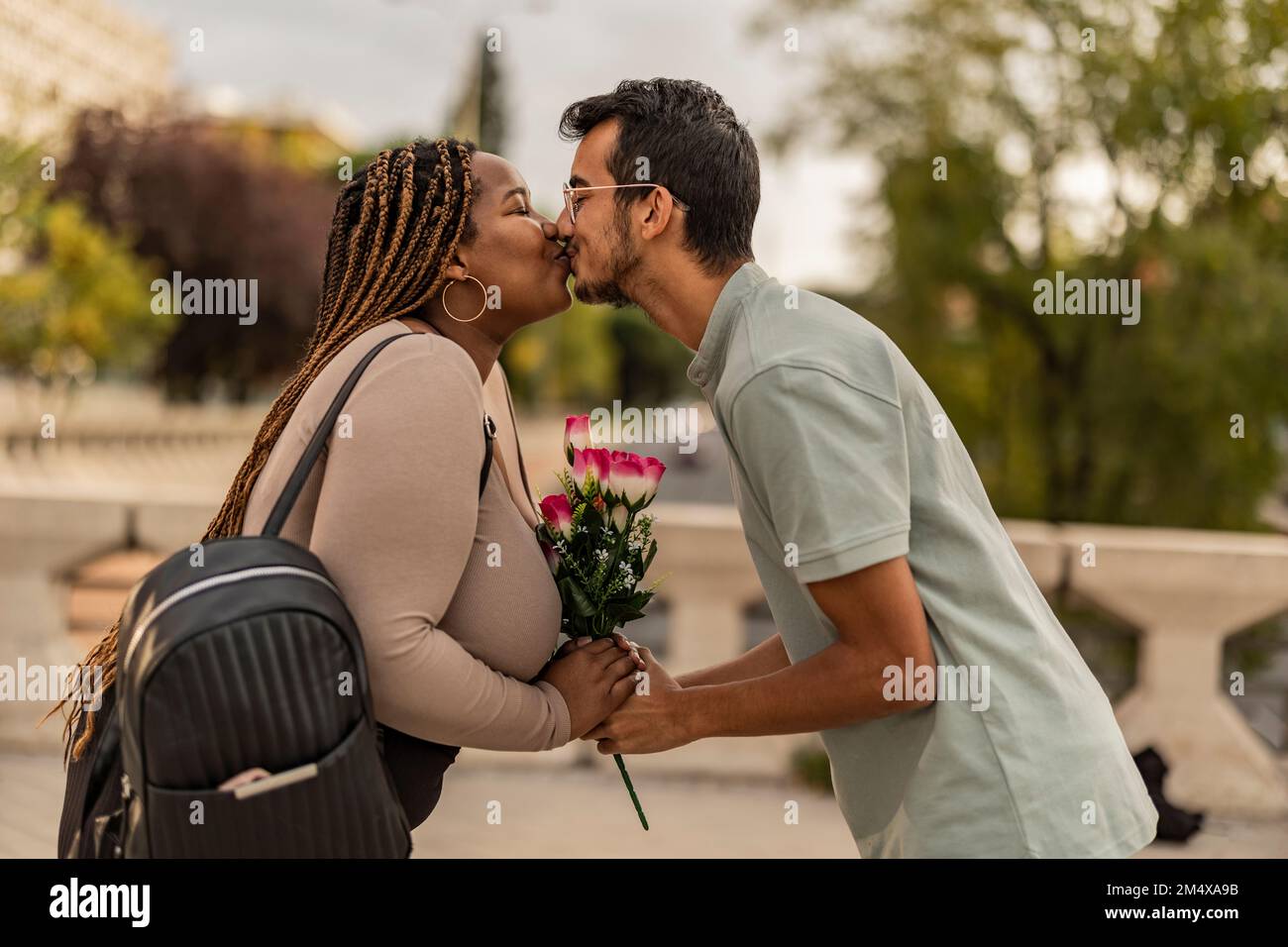 Young couple kissing each other with bouquet of flowers at footpath ...
