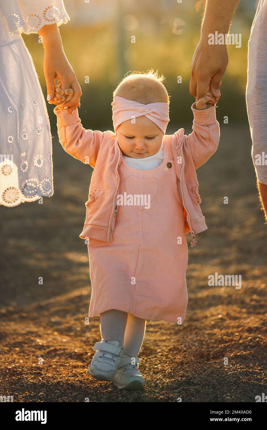 Cute baby girl holding hands and walking with parents Stock Photo Alamy
