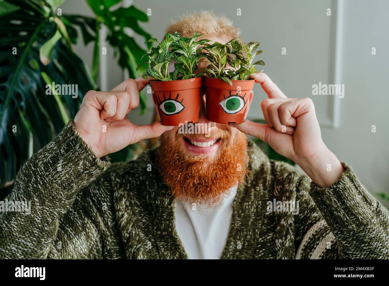 Happy man holding potted plants with eyes at home Stock Photo - Alamy