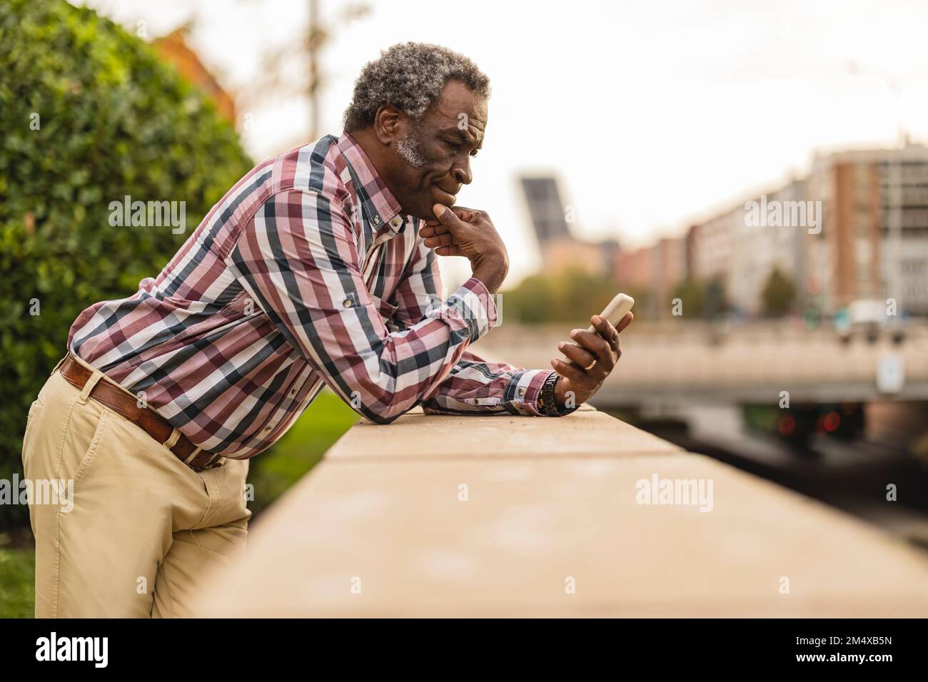 Thoughtful man using smart phone leaning on wall Stock Photo