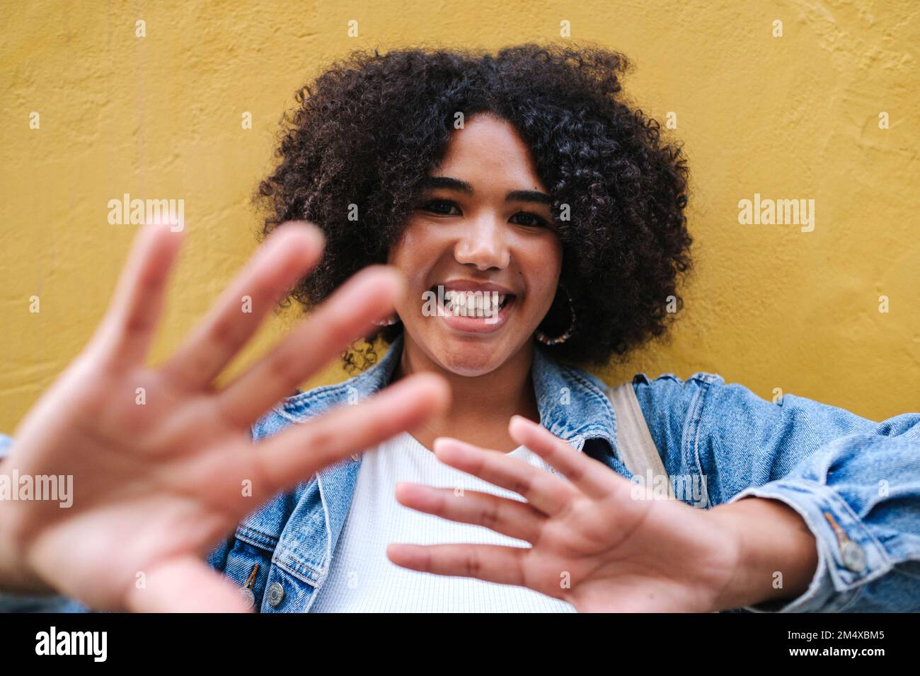 Smiling young woman gesturing in front of yellow wall Stock Photo - Alamy