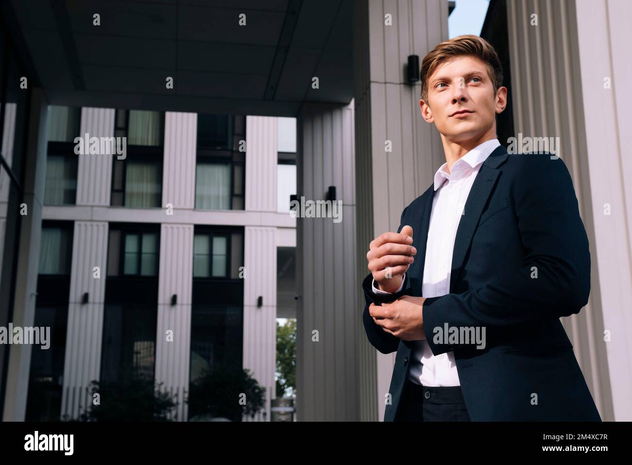 Young businessman adjusting cuff button standing in front of building Stock Photo