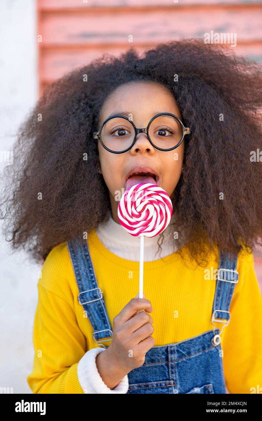 Cute girl wearing eyeglasses licking lollipop Stock Photo