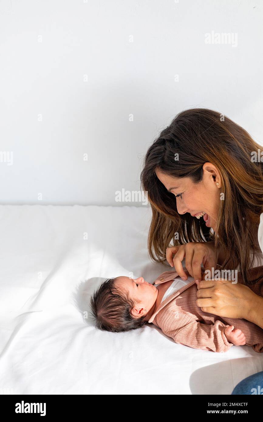 Mother playing with newborn daughter lying on bed at home Stock Photo