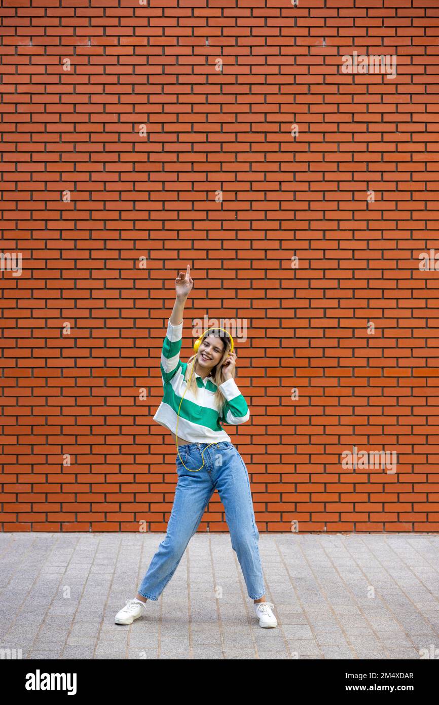 Happy young woman listening to music through headphones dancing on ...