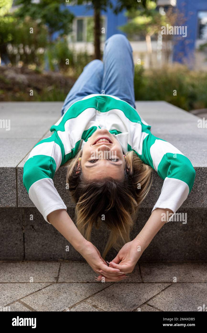 Happy young woman lying on concrete bench Stock Photo