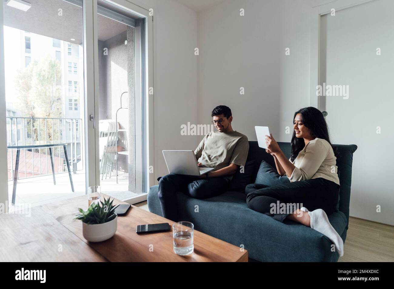 Young man and woman studying using laptop and tablet PC on sofa in living room Stock Photo