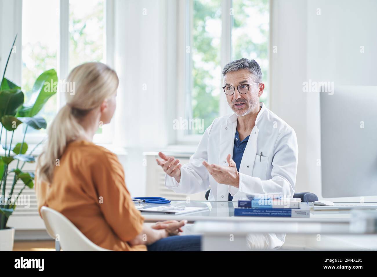 Doctor discussing with patient sitting at desk in medical practice ...