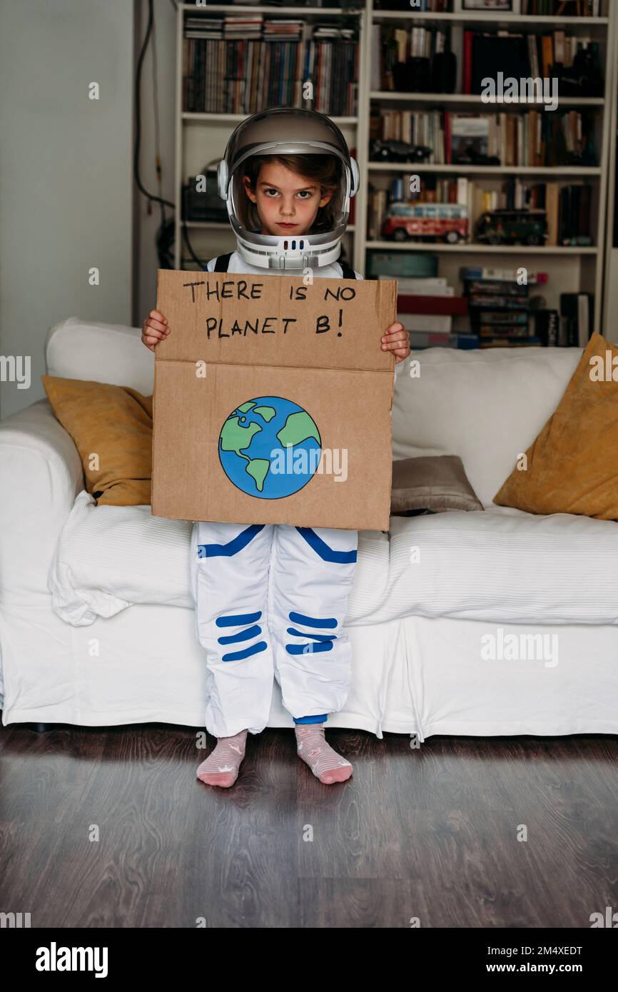 Girl wearing space costume holding banner with message in front of sofa at home Stock Photo
