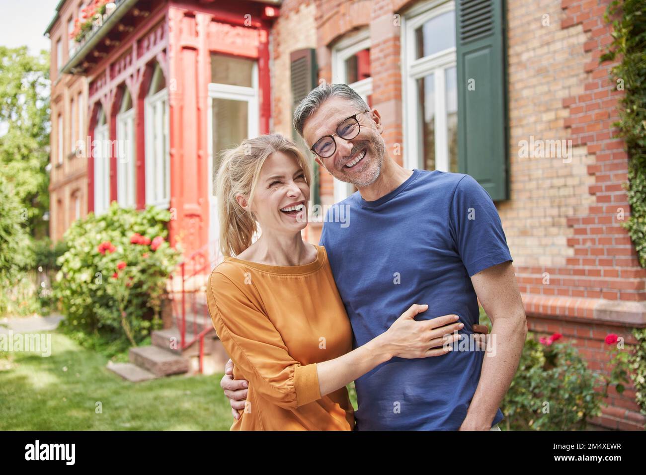 Happy woman embracing man in front of house Stock Photo