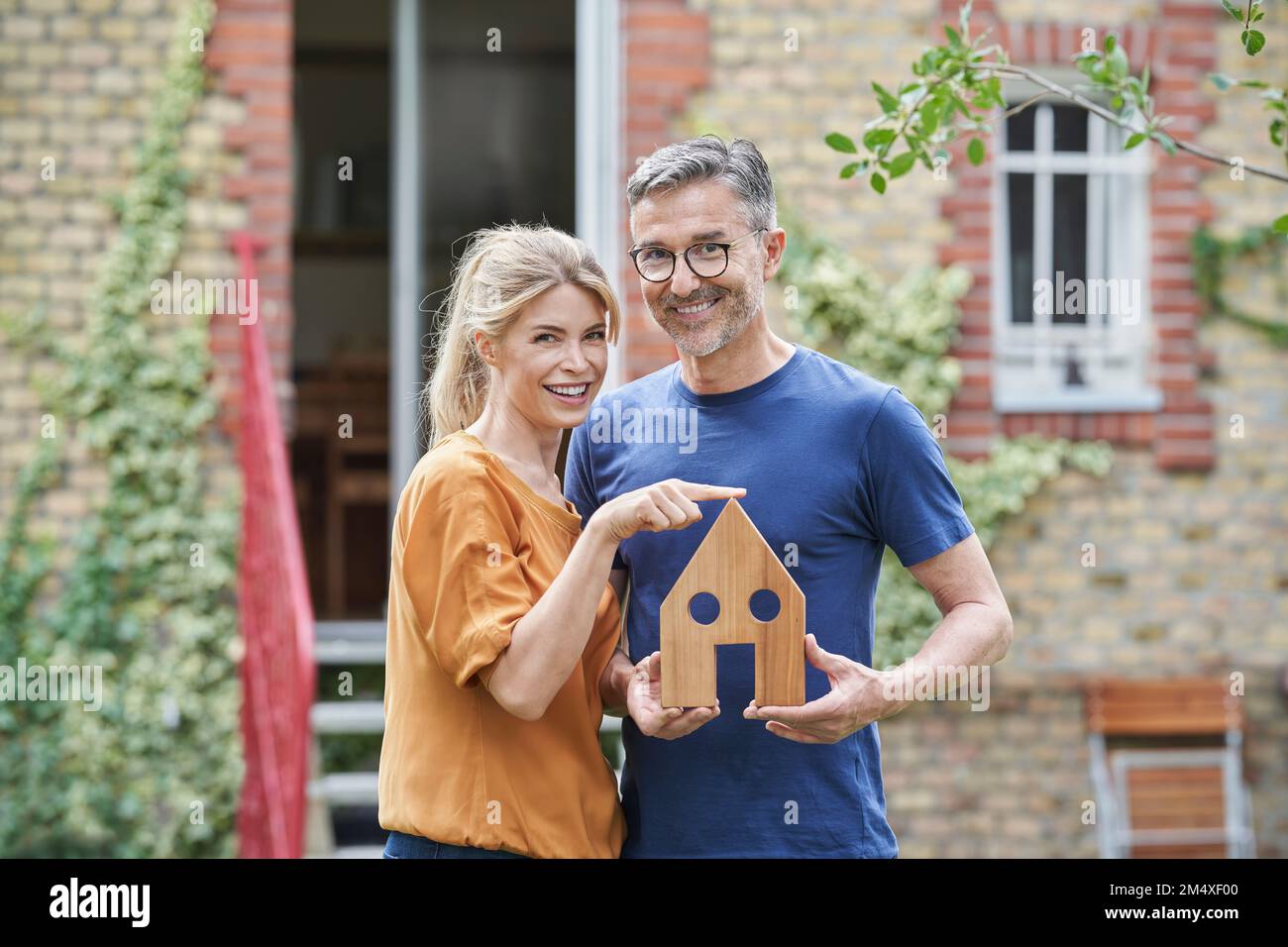 Happy man holding wooden house model by woman in garden Stock Photo - Alamy