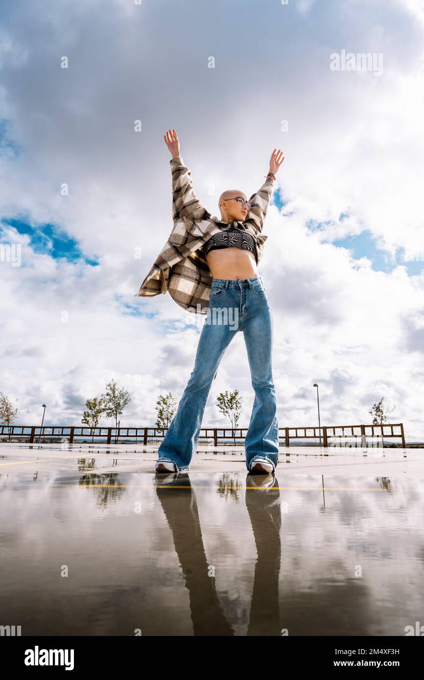 Woman standing with arms raised in front of cloudy sky Stock Photo