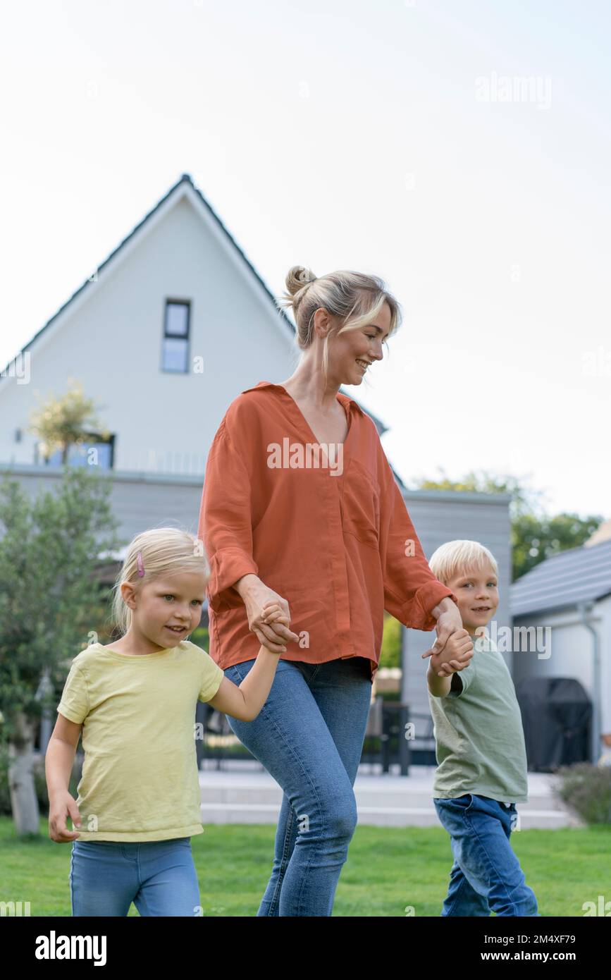 Smiling woman holding children's hand walking in garden Stock Photo