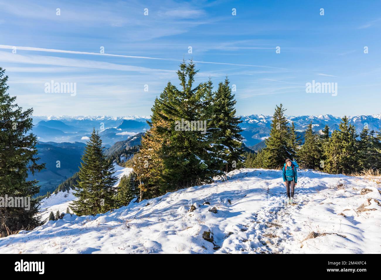 Germany, Bavaria, Female hiker walking through snow-covered mountaintop in Chiemgau Alps Stock Photo