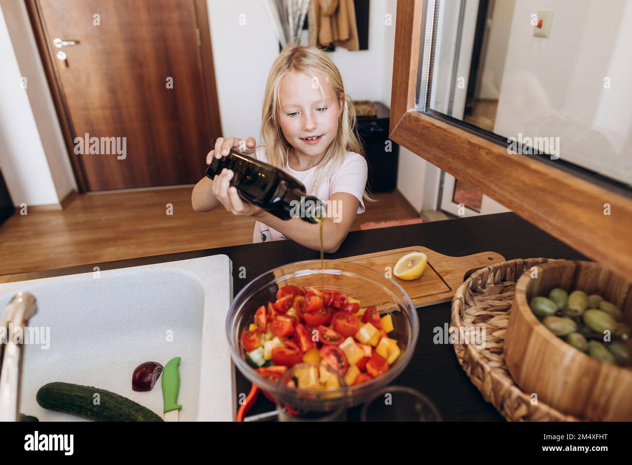 Girl preparing a salad in the kitchen pouring oil into bowl Stock Photo