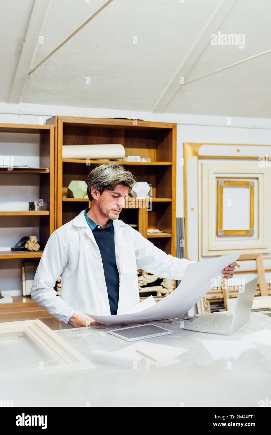 Mature craftsman looking at blueprint in workshop Stock Photo - Alamy