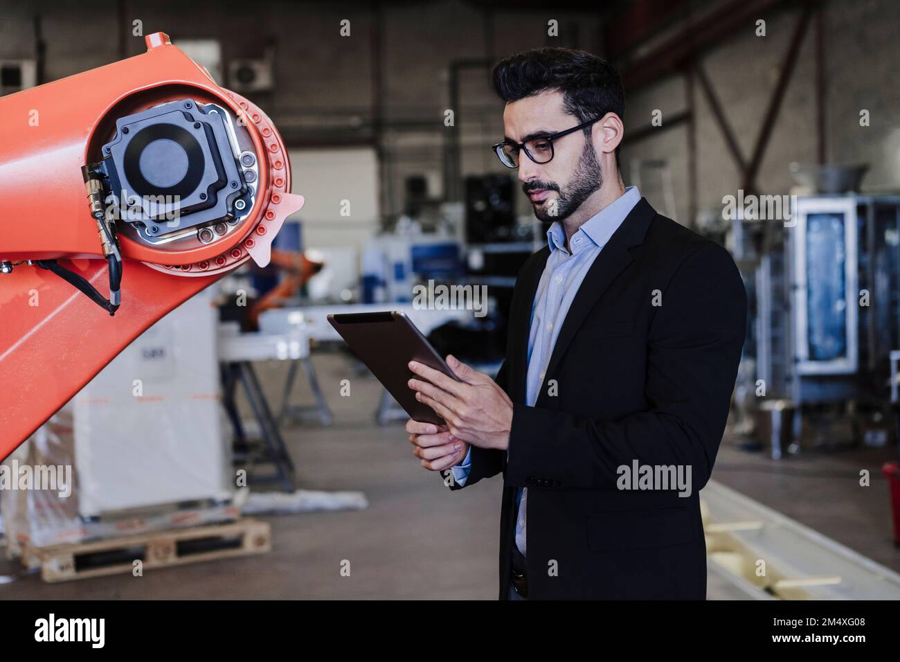 Engineer using tablet PC standing by robotic arm in industry Stock Photo