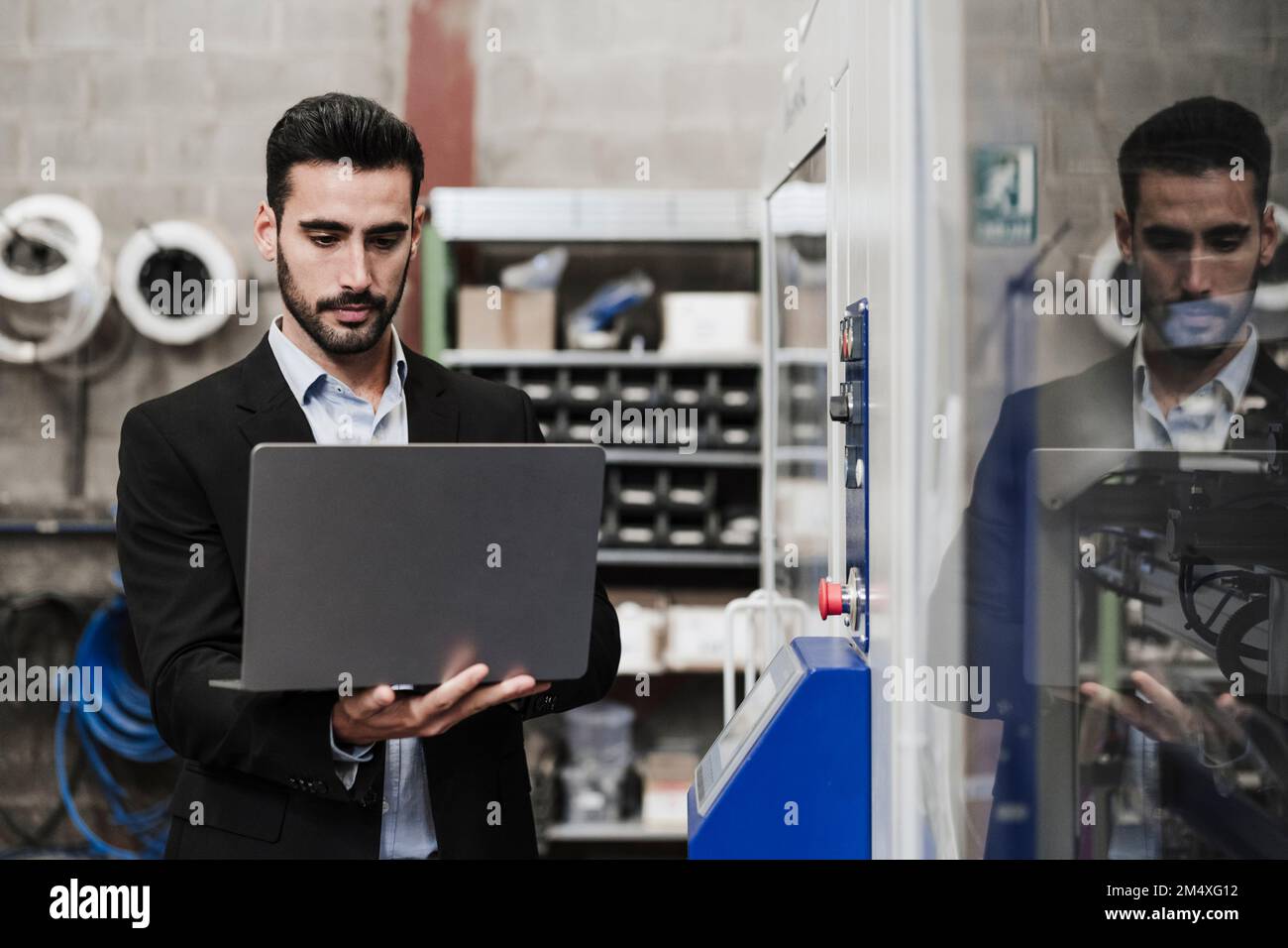 Engineer using laptop standing by machinery at industry Stock Photo