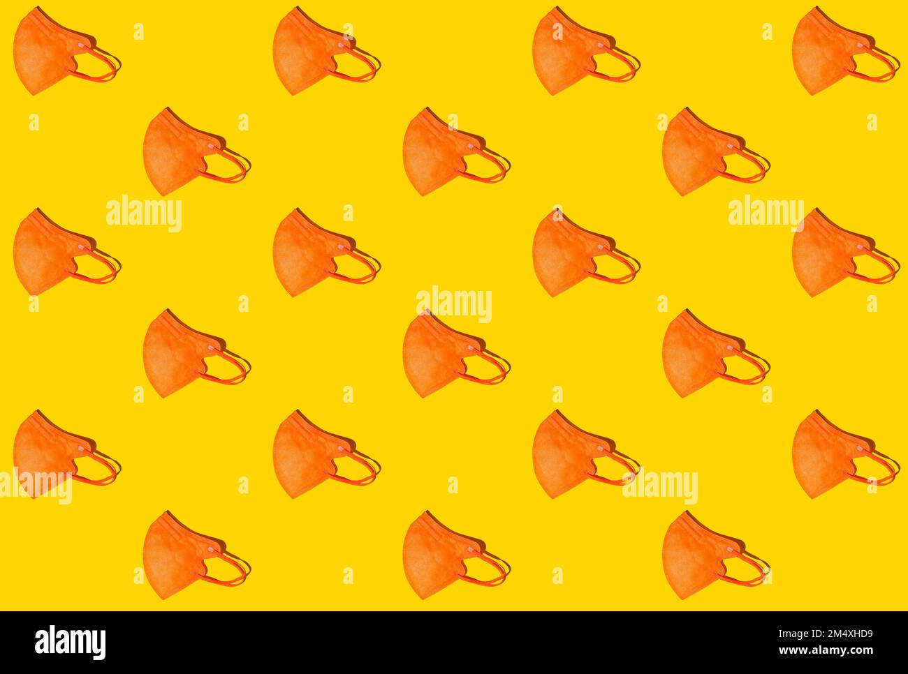 Pattern of rows of orange colored FFP2 masks flat laid against yellow background Stock Photo