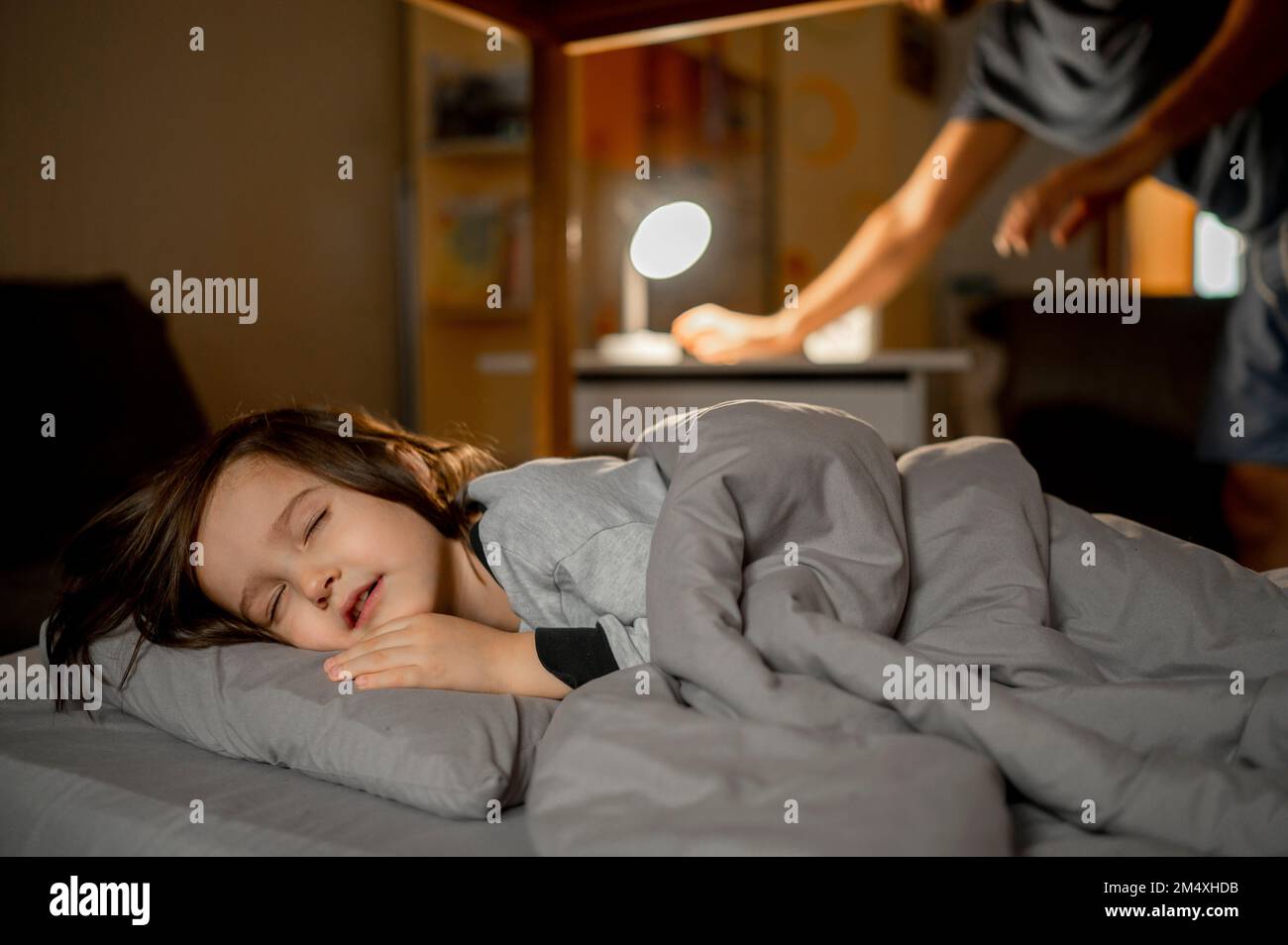 Son sleeping on bed with father putting lights off in background Stock