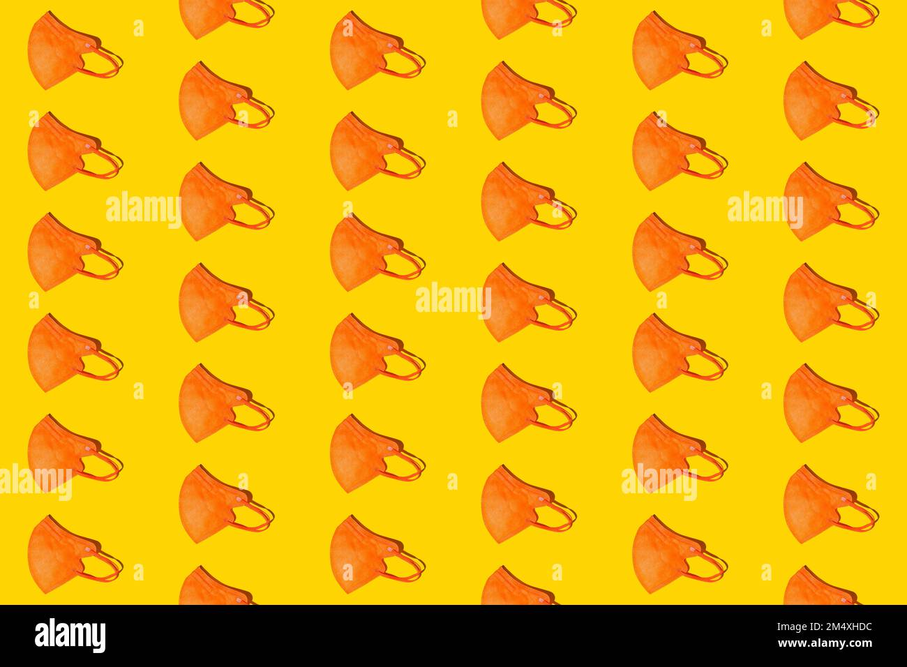 Pattern of rows of orange colored FFP2 masks flat laid against yellow background Stock Photo