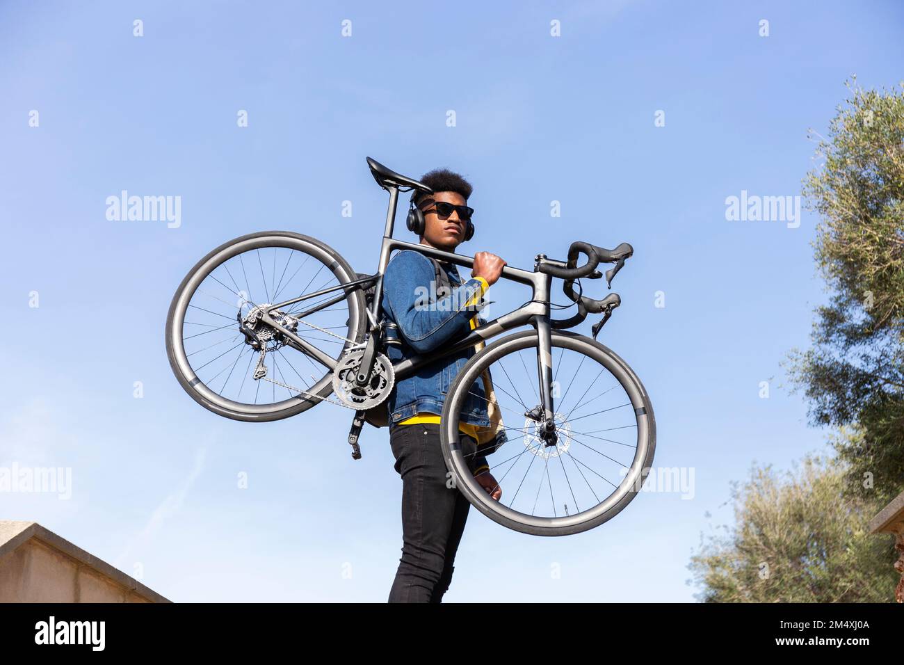 Young man carrying bicycle under clear blue sky Stock Photo