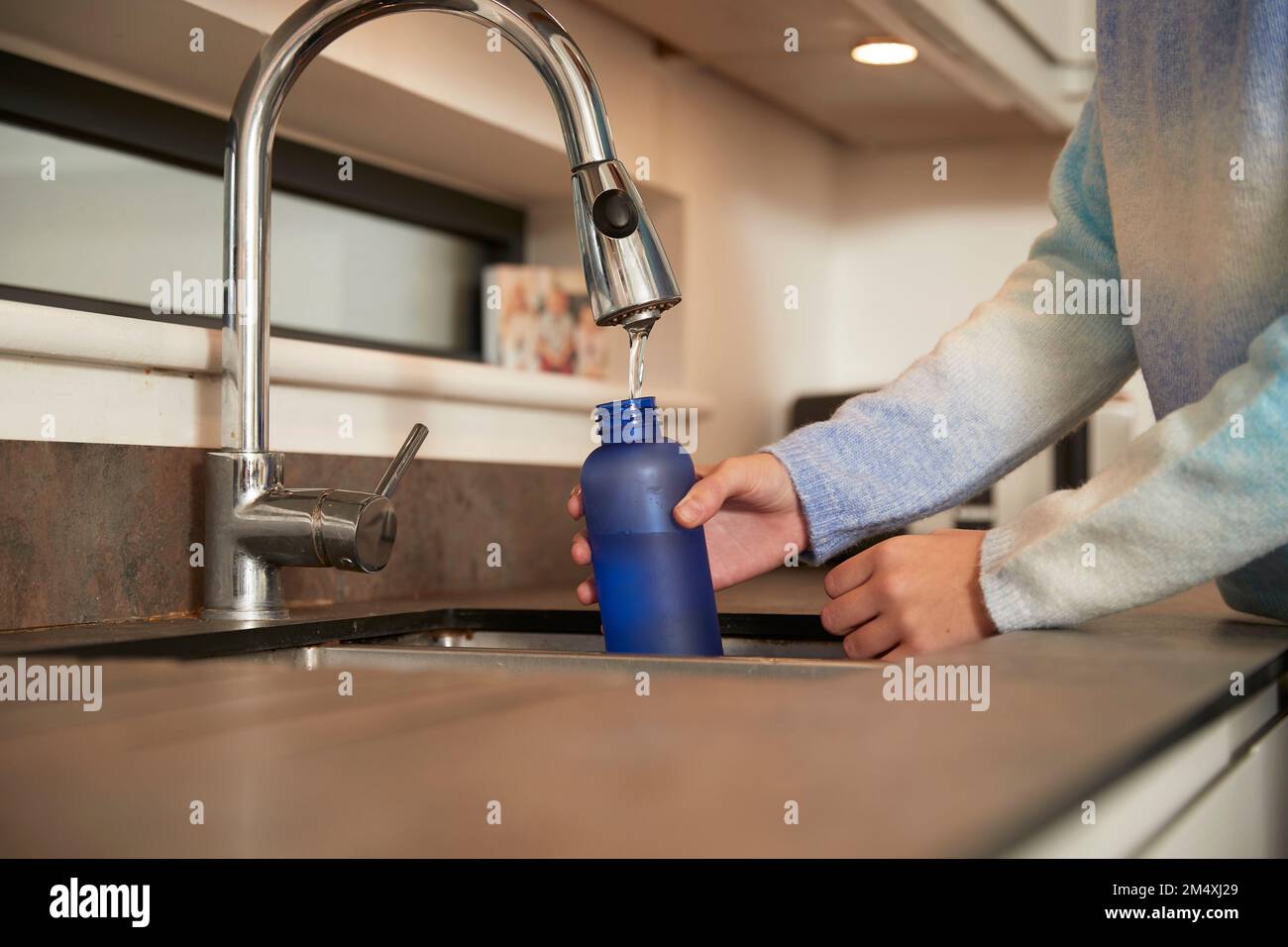 Girl filling reusable bottle with water from faucet Stock Photo