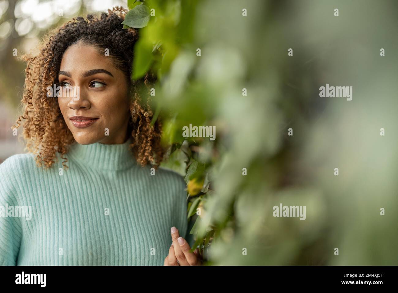 Beautiful young woman with curly hair by plants Stock Photo - Alamy