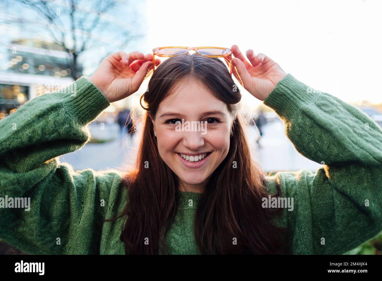 Happy woman wearing green sweater adjusting sunglasses on head Stock Photo