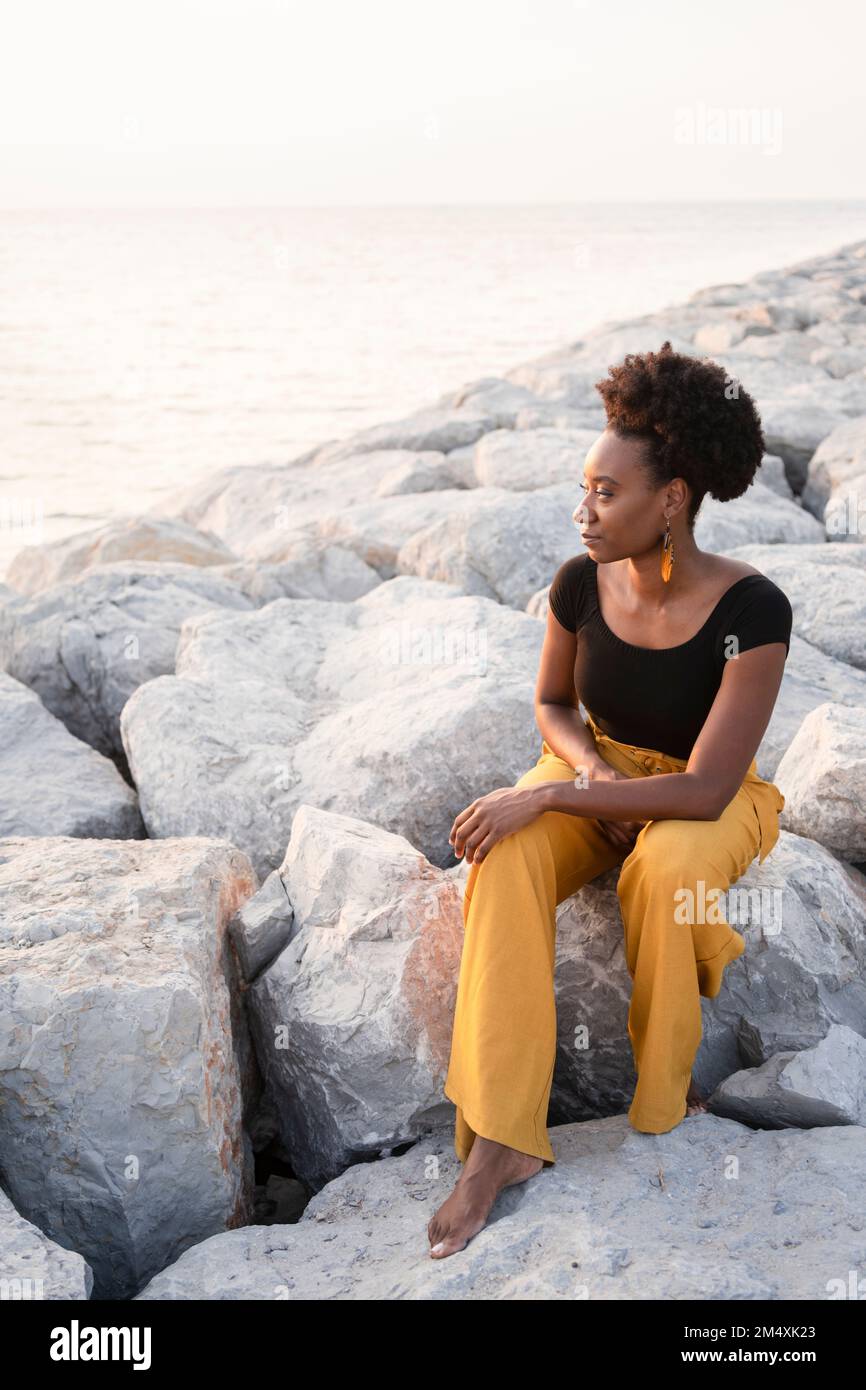 Woman sitting on rocks and looking at sea Stock Photo