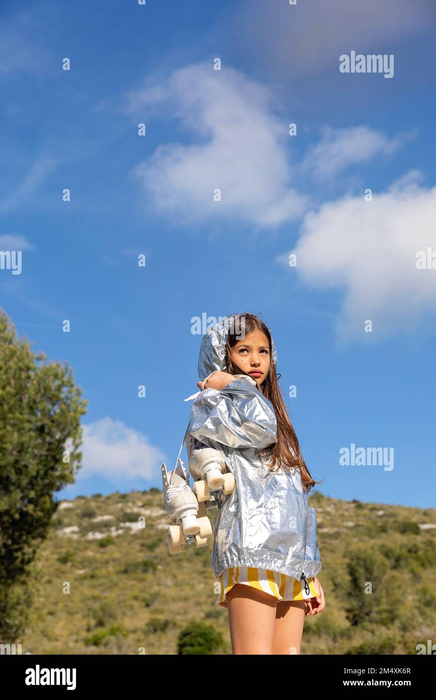 Girl in silver jacket standing with roller skates on mountain under blue sky Stock Photo