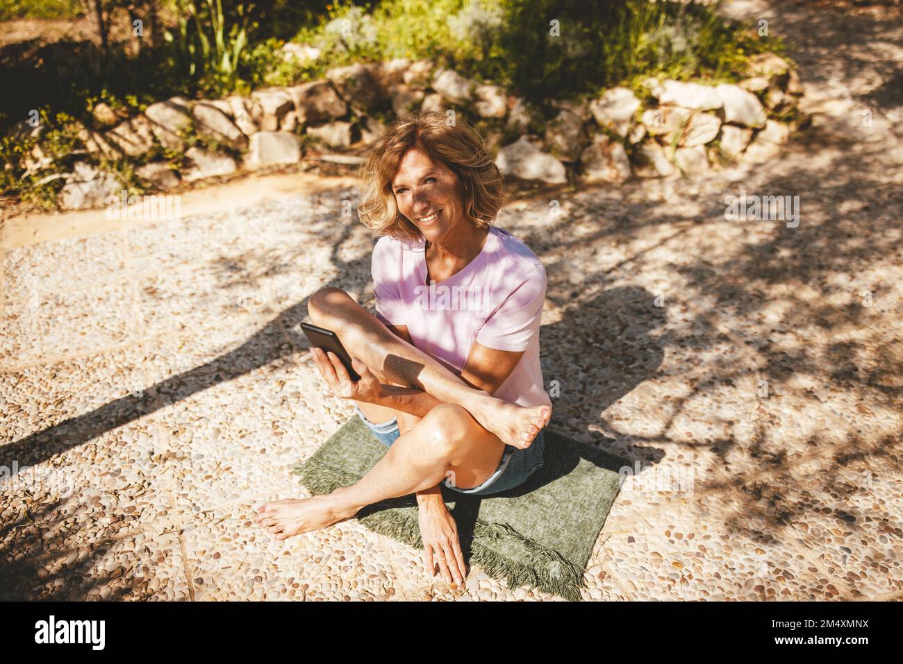 Happy mature woman practicing yoga with smart phone in back yard Stock Photo