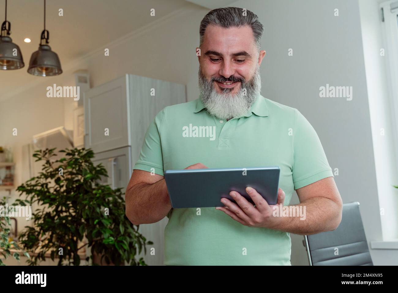 Smiling mature bearded man using tablet PC at home Stock Photo