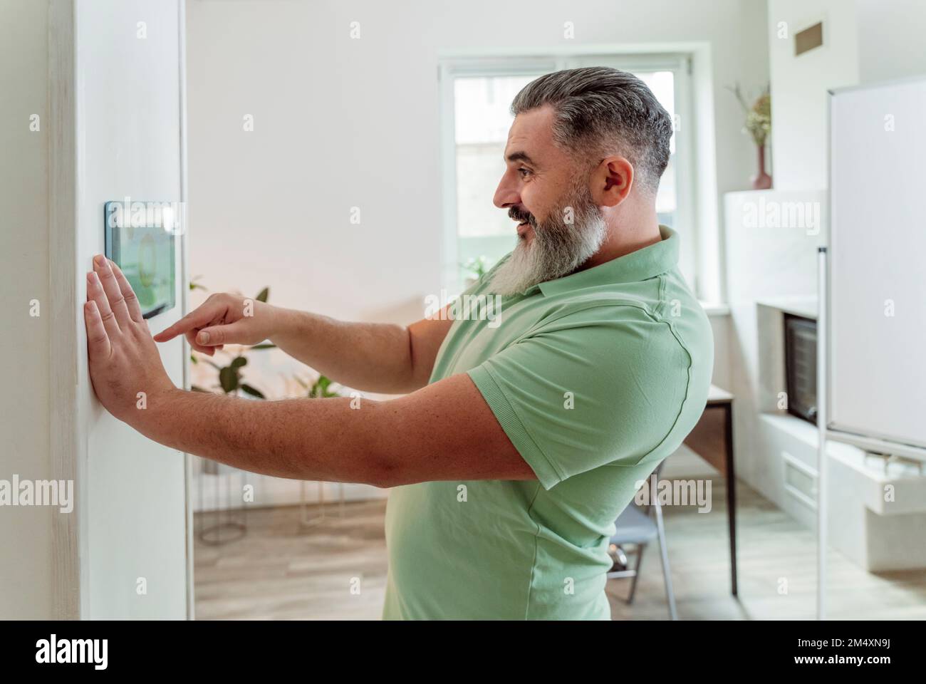 Smiling man using smart home application through tablet PC mounted on wall Stock Photo