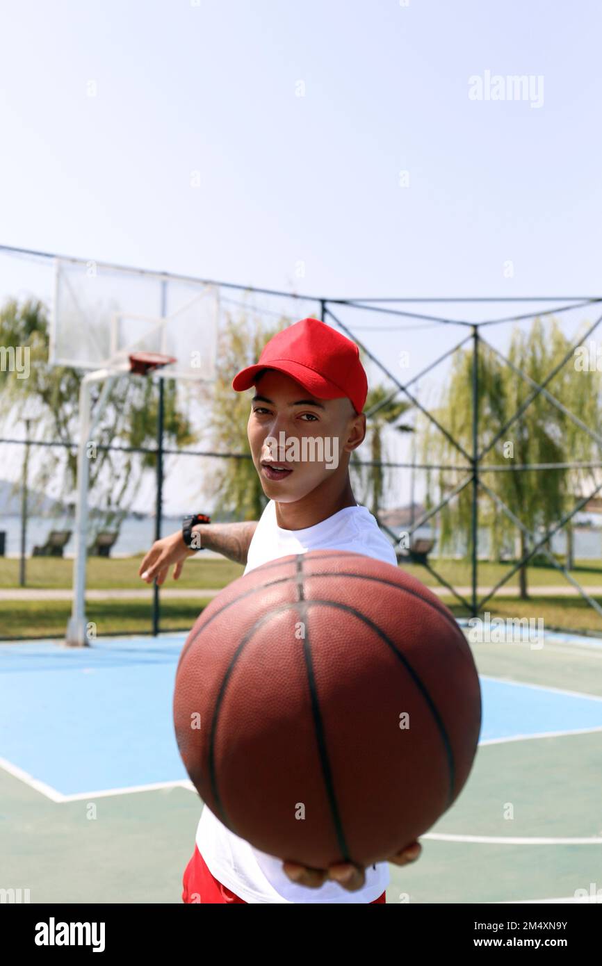 Young man wearing cap holding basketball at sports court Stock Photo