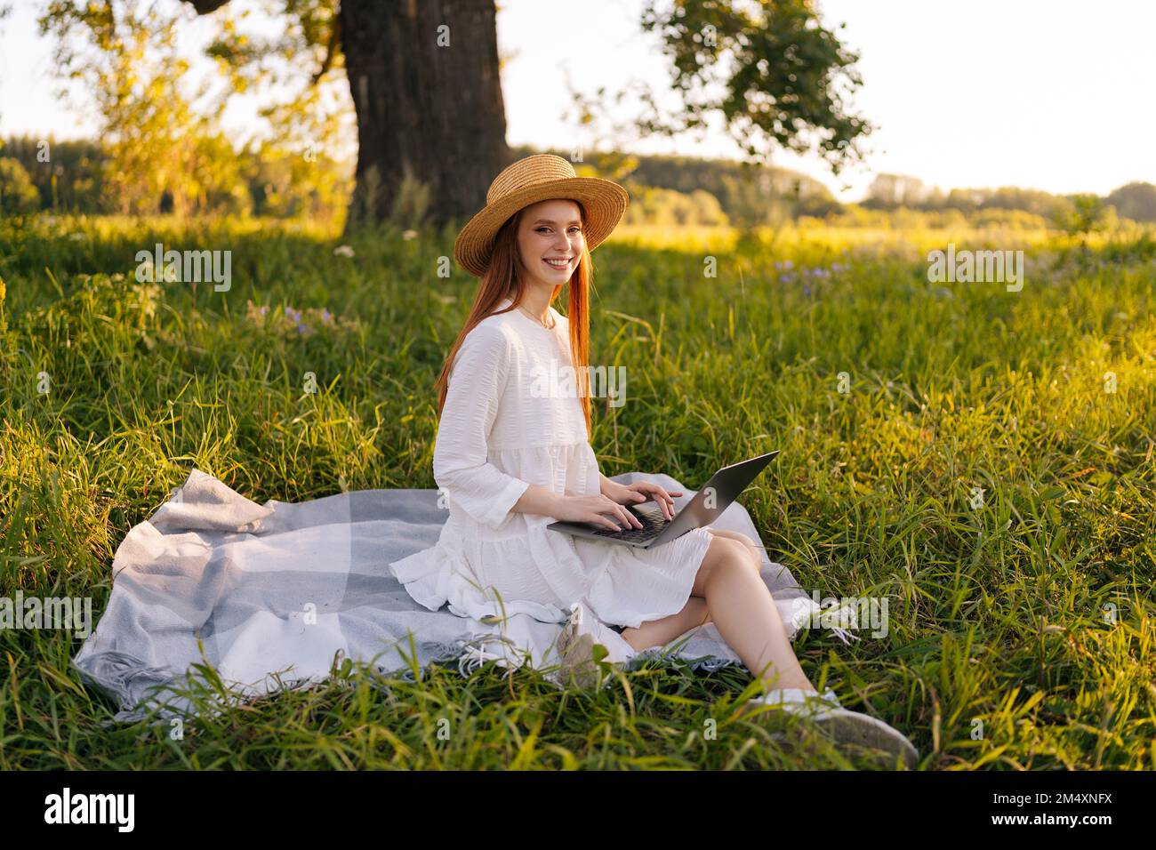Portrait of cheerful young ginger female freelancer in straw hat and ...