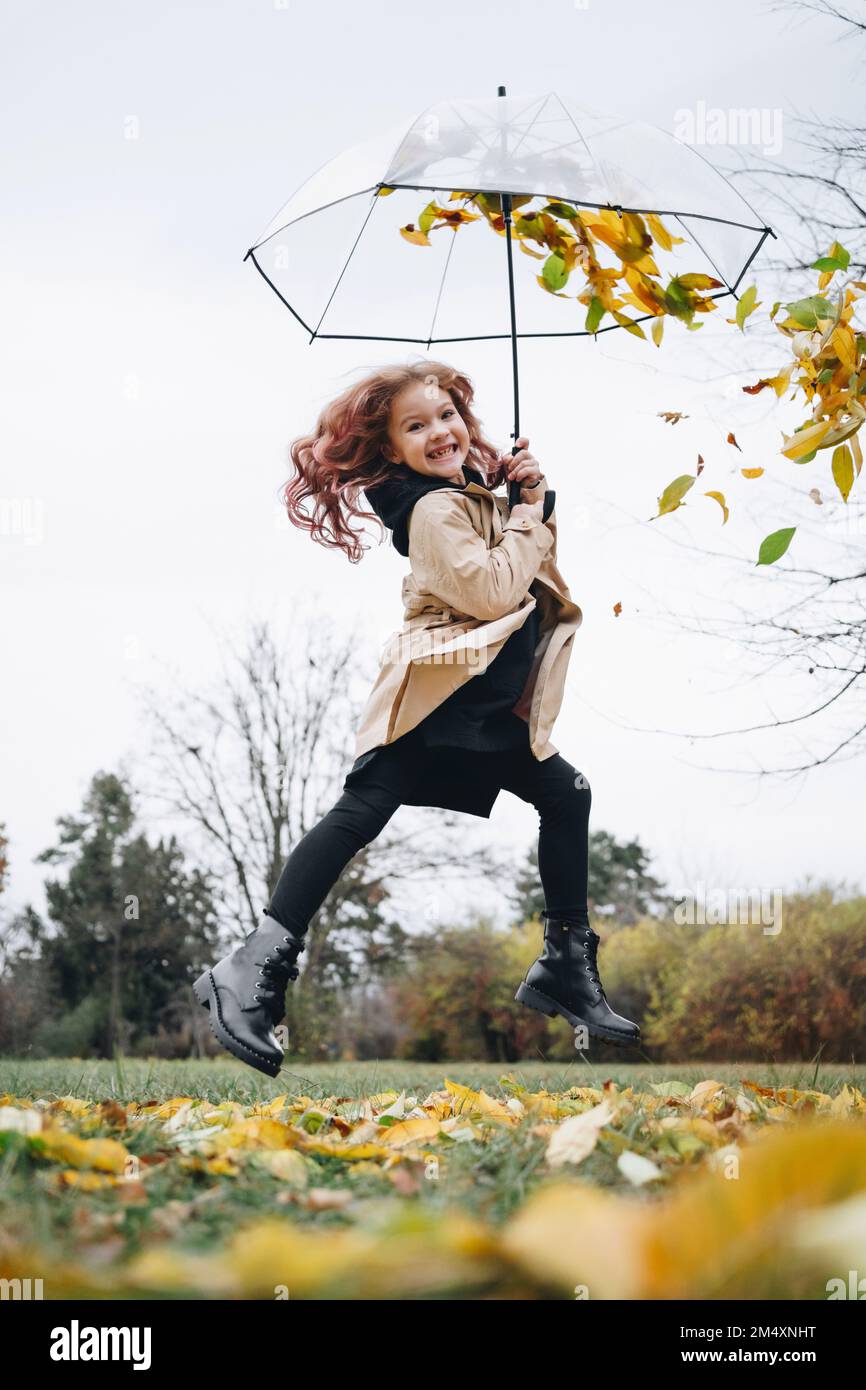 Cheerful cute girl jumping with umbrella in park Stock Photo - Alamy
