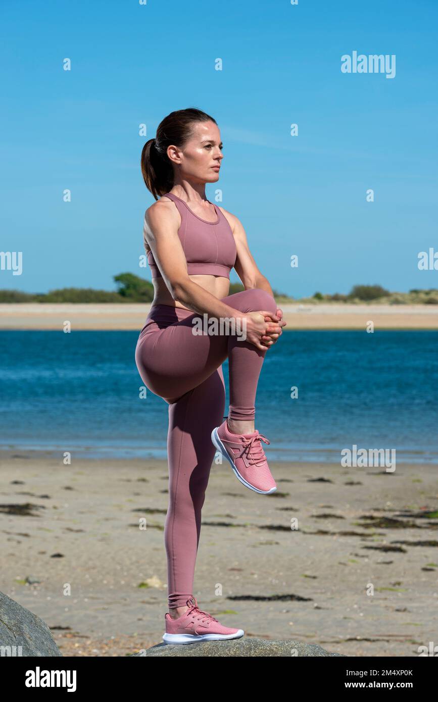 Fit sporty woman doing a leg stretch while exercising at the beach. Stock Photo