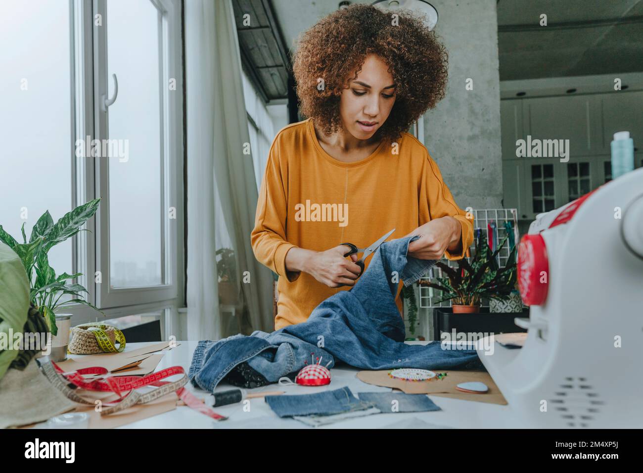 Fashion designer cutting jeans with scissors in Stock Photo