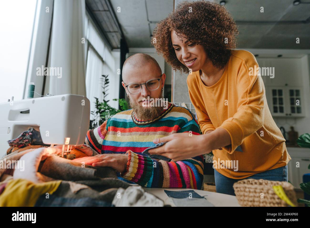 Smiling fashion designer showing denim fabric to colleague in workshop ...