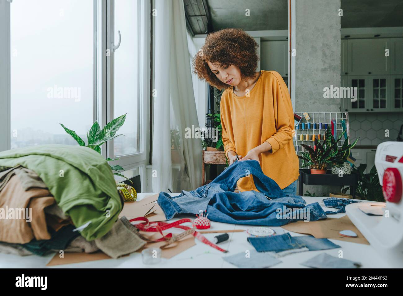 Young fashion designer cutting jeans with scissors in Stock
