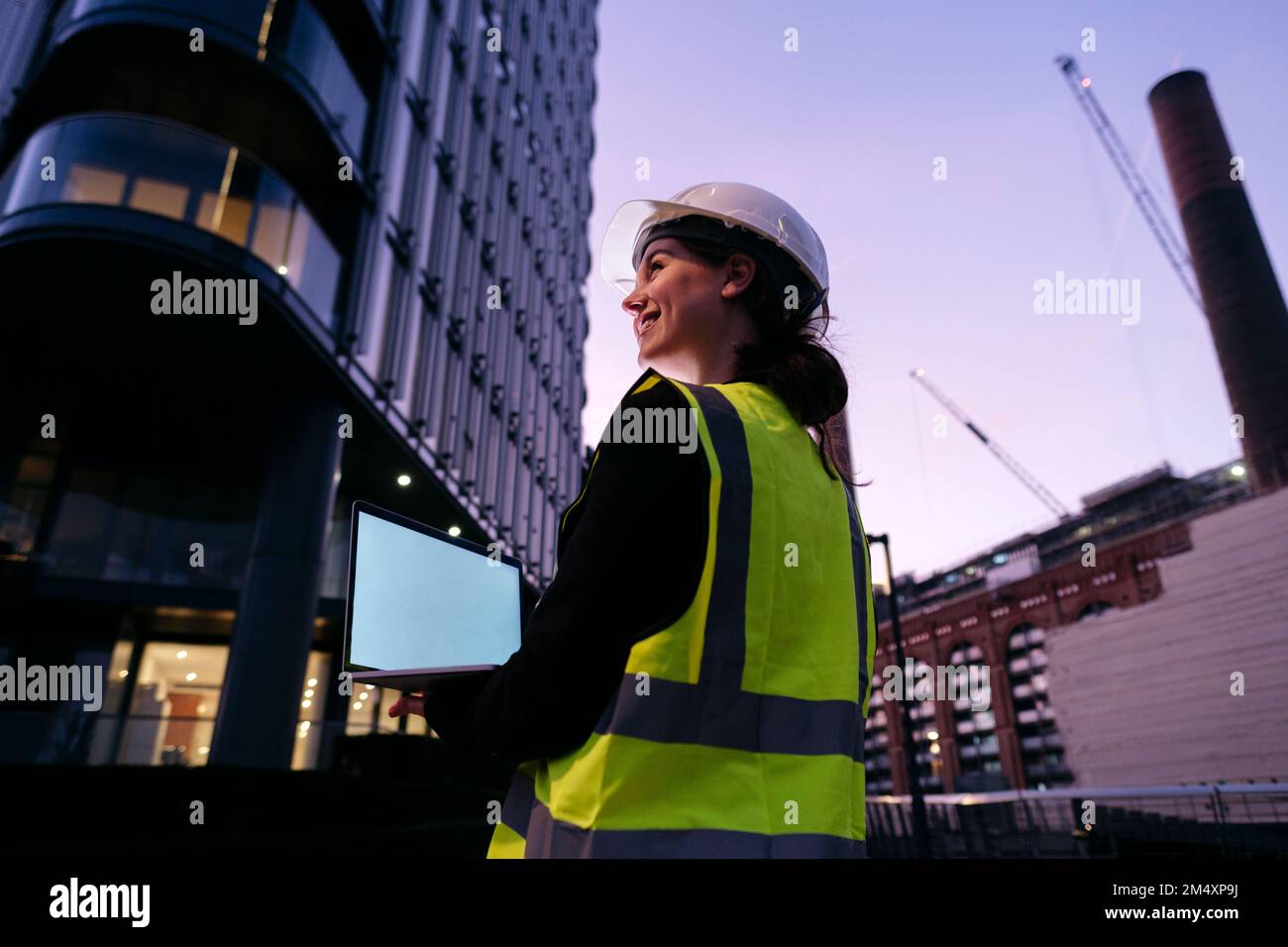 Smiling young engineer holding laptop at dusk Stock Photo