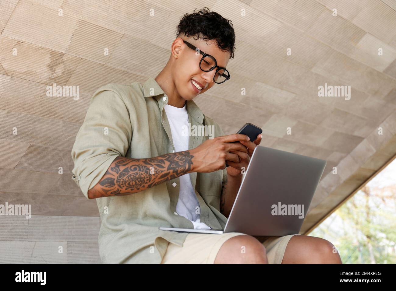 Happy freelancer using smart phone sitting with laptop Stock Photo