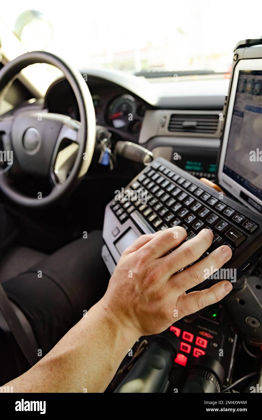 White male police officer hand and fingers typing on keyboard in cop vehicle searching for information to better help make informed decision to pull s Stock Photo