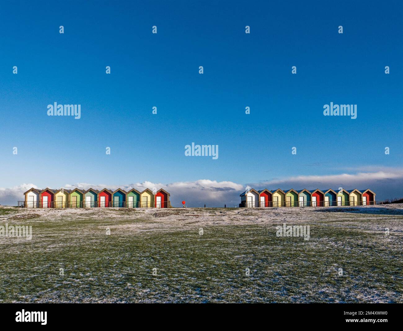 Beach huts at Blyth, Northumberland, UK with blue sky background and frosty links grass in the foreground Stock Photo