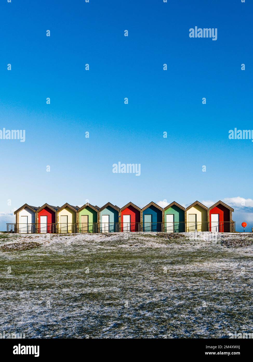 Beach huts at Blyth, Northumberland, UK with blue sky background and frosty links grass in the foreground Stock Photo