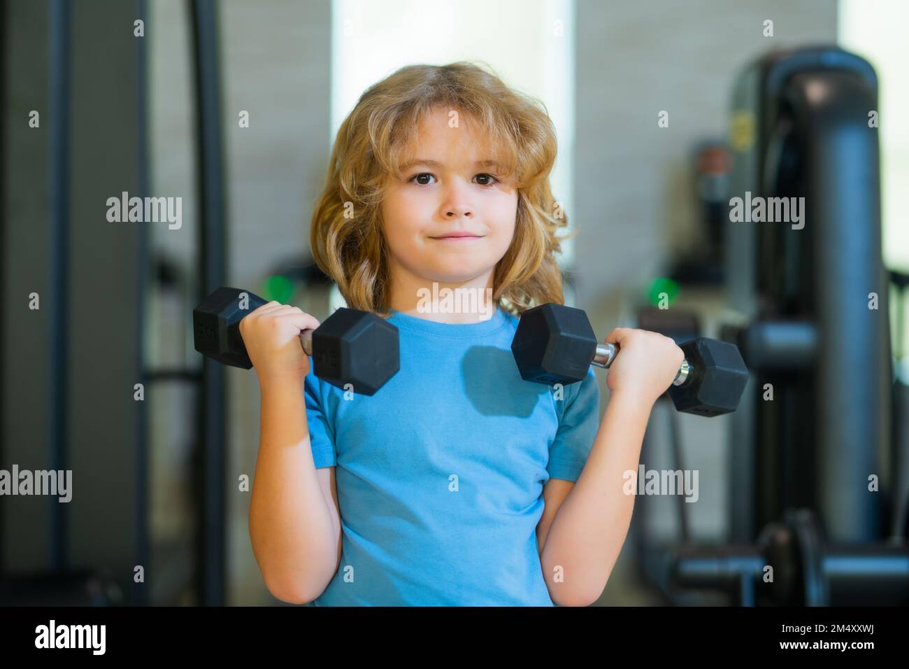 Sport activities at leisure with children. Blonde boy holding dumbbells. Sports exercises for children. Funny child lifting the dumbbells. Stock Photo