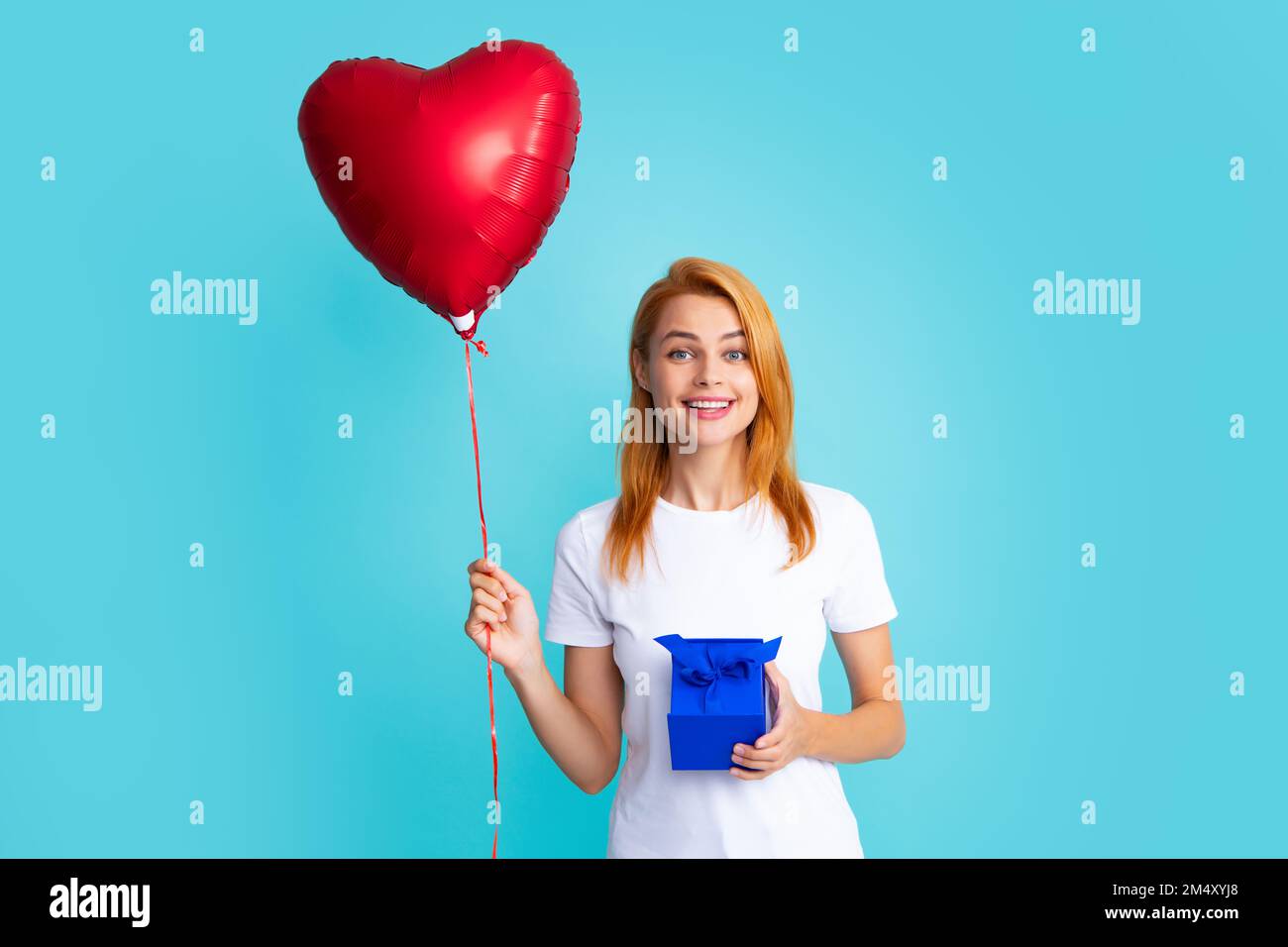 Attractive woman with present box posing with surprised face expression on gray background. Girl holding gift decorated with ribbon. Valentine day Stock Photo