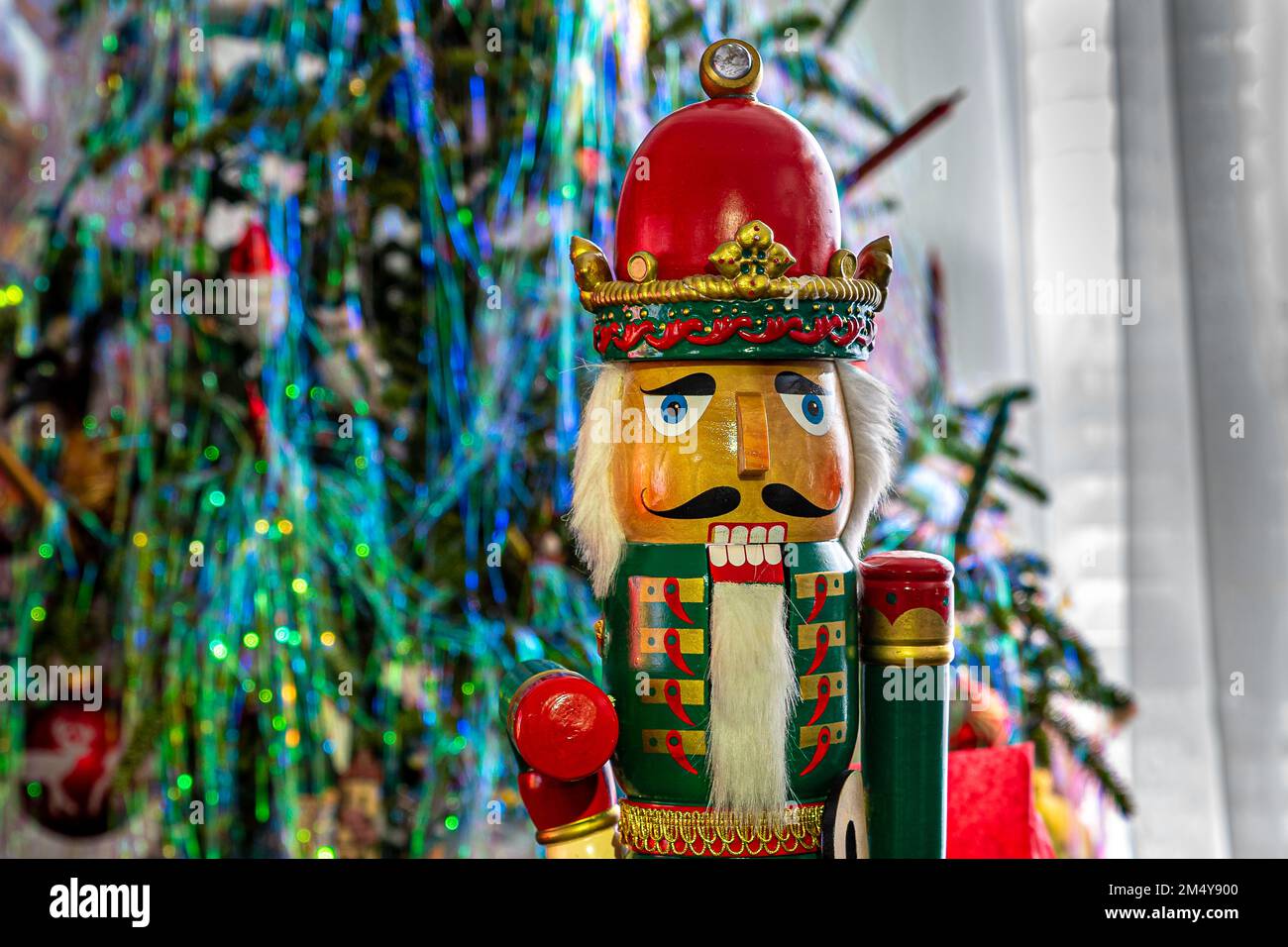 Nutcracker standing wooden soldier, iconic nutcracker. Standing against the background of a Christmas tree. Stock Photo